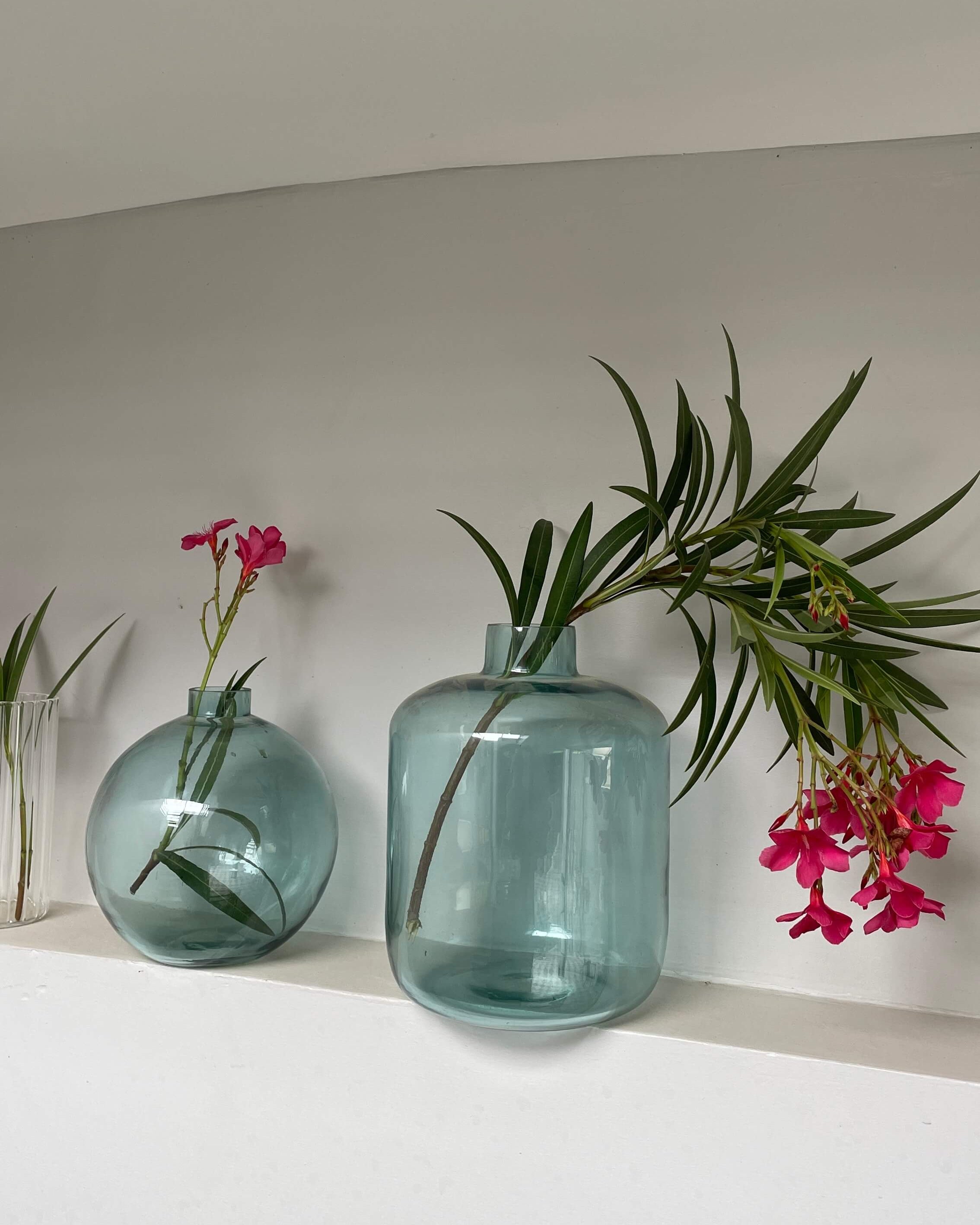 Two blue glass vases with greenery and pink flowers on a white surface.