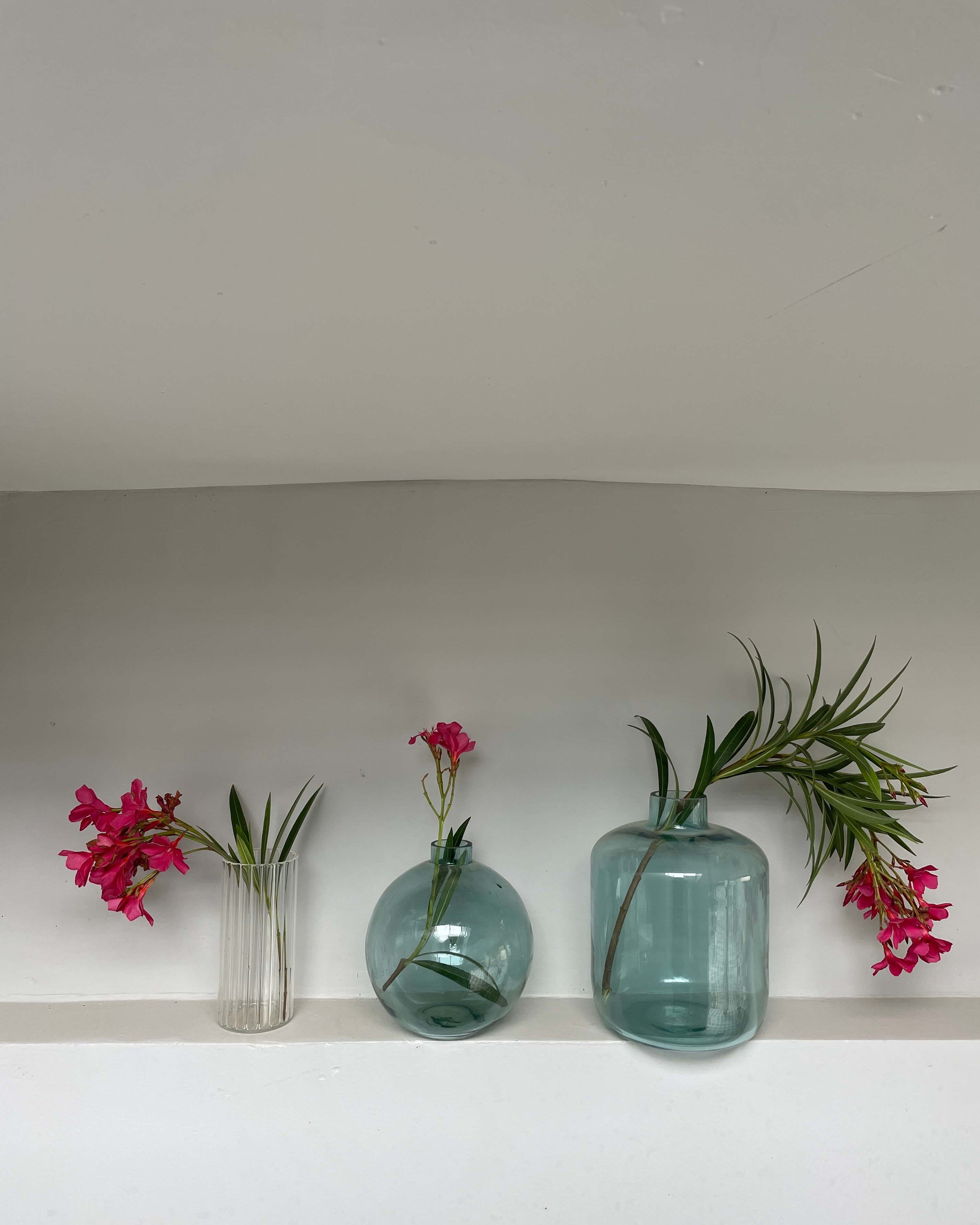 Three glass vases with pink flowers and greenery on a white surface.